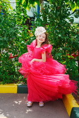 A girl in a lush pink dress and hat near the green bushes