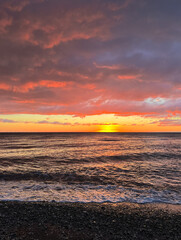 Vivid sunset over the sea with colourful clouds and gentle waves washing the pebble shore
