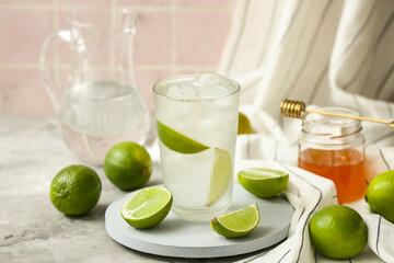 Glass of lime infused water and jar of honey on grey table