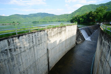 Spillway of a Concrete Weir Dam in Thailand, Contrasting Water Infrastructure with Lush Tropical Green Mountains.