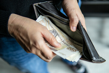 Close-up of a person pulling out a 200 PLN banknote from a wallet. The photo illustrates financial transactions