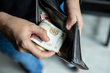 Person holding a 200 PLN banknote near an open leather wallet. Image symbolizes cash handling, personal finances