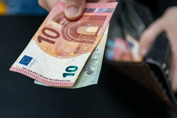 A hand holding euro banknotes (10 and 5 EUR) over an open wallet. Symbol of daily spending, European economy, travel expenses