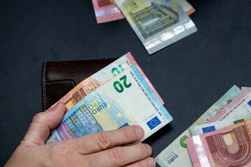 A hand holding euro banknotes (20 and 10 EUR) with scattered bills on a dark surface. Concept of cash payment, budgeting, travel, or currency exchange in the eurozone.