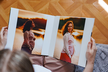 woman is holding and flipping through a photo book with a pregnancy photo shoot