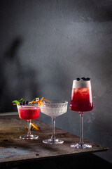 Three artisanal cocktails with berry and citrus garnish on moody metal surface