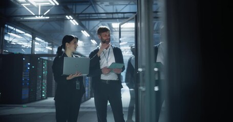 Technicians examine server racks in data center, using a laptop and tablet to check system performance, troubleshoot network issues, monitor equipment status in rows of server mainframe racks - Powered by Adobe