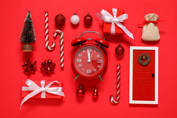 Alarm clock with Christmas decorations and gift boxes on red background
