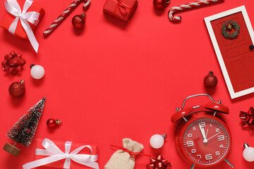 Frame made of alarm clock with Christmas decorations and gift boxes on red background