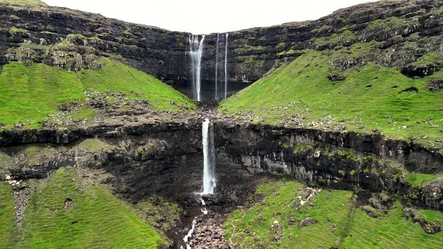 Fossa waterfall captivates with its stunning two-tiered cascade, surrounded by lush green hills and dramatic cliffs. This enchanting location in the Faroe Islands showcases natures beauty.