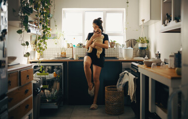 Mother holds baby in bright kitchen with plants