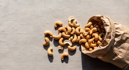 Roasted Cashew Nuts Spilling from Brown Paper Bag onto Fabric Surface