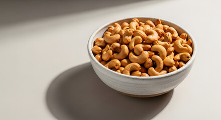 White ceramic bowl of roasted cashew nuts on light surface