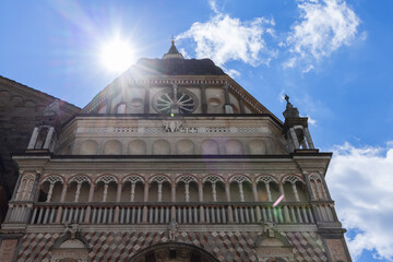 Facade of the Colleoni Chapel in Bergamo Lombardy, upward view captures Renaissance marble architecture glowing under sunlight with rose window arches and radiant geometric design