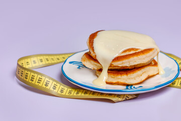 Pancakes with buttercream on a plate, measuring tape around, the concept of losing weight and breaking a diet on a purple background