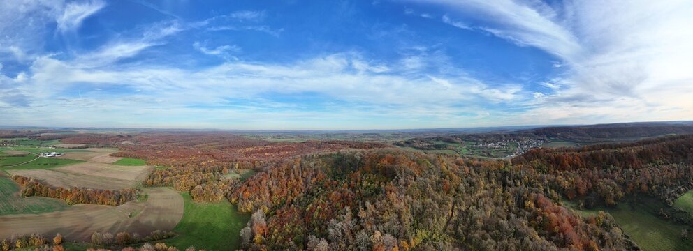 vue a&eacute;rienne panoramique sur les champs et les for&ecirc;ts en automne. Les arbres ont encore des feuilles multicolores, les champs t les prairies sont verte avec un ciel bleu et des nuages stratus blancs.