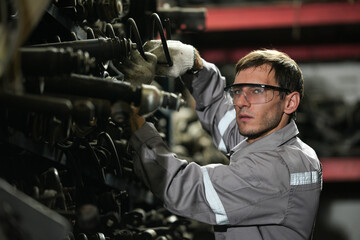 Professional auto mechanic worker using tools for car engine repair service in a garage workshop. Maintenance technician with junk motor part in vehicle junkyard