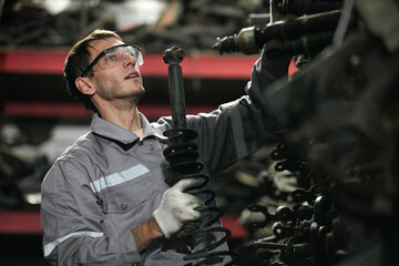 White man technician examines used car damaged engine block at scrap yard warehouse recycle area...