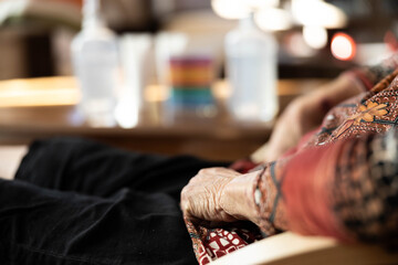 The hands of an elderly woman resting on her lap signify a moment of contemplation and self-care while products lie in the background, conveying a sense of warmth and tenderness.