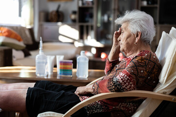 The elderly woman reflects on her life experiences, resting comfortably in her chair, showcasing a serene expression against the backdrop of her inviting and cozy living room.