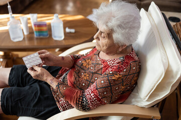 This image presents an elderly woman engaged with a pack of medication, illustrating her as a symbol of resilience and the importance of health management in a nurturing home atmosphere.