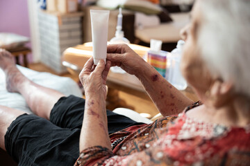An elderly woman examines a tube of cream while seated, showcasing the significance of care in her daily routine. The image captures the essence of personal health care among seniors.