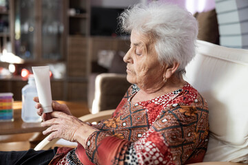 A senior woman seated in a cozy environment, thoughtfully examining a tube of lotion. The warm lighting highlights her skin, emphasizing the importance of moisturizing in older age.
