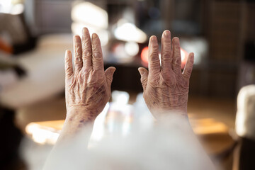 Two aging hands lifted towards natural light, revealing detailed textures and age spots, symbolizing the passage of time and the beauty found in the hands of the elderly.