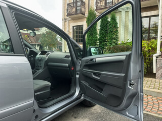Exploring the interior of a silver car parked near a cozy building surrounded by greenery on a bright day