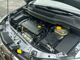 Car engine in detail showing various components and systems under the hood during a routine maintenance check in a driveway
