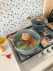 Vegetable broth is cooked at home in kitchen. Pot with lid on gas stove. Healthy eating.