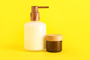 Soap dispenser and jar of cream on yellow background