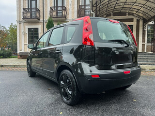 Sleek black compact car parked elegantly in front of a stylish building during a cloudy afternoon