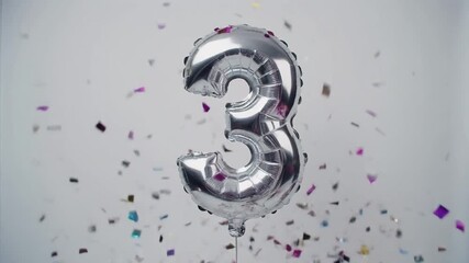 Silver balloon number 3 for birthday or anniversary party. White background with falling confetti
