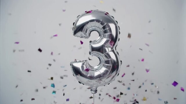 Silver balloon number 3 for birthday or anniversary party. White background with falling confetti