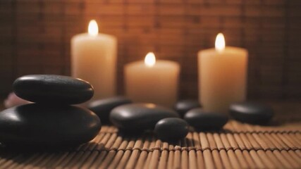 Stacked smooth dark massage stones illuminated by soft candlelight on bamboo matting - Powered by Adobe