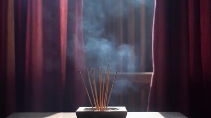 Incense sticks burning and releasing fragrant smoke in front of dark red drapery - Powered by Adobe