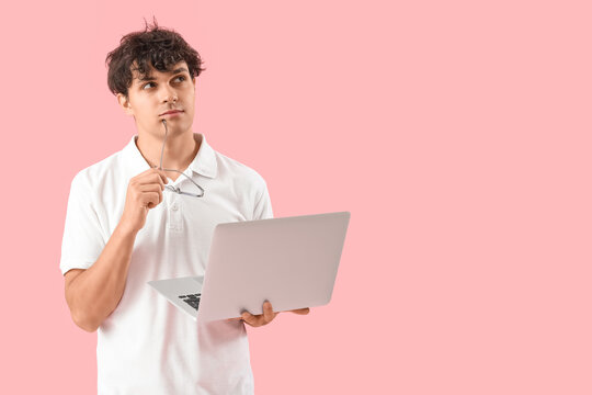 Thoughtful male programmer with eyeglasses and laptop on pink background