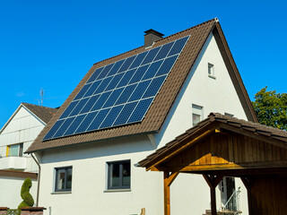 Solar panels installed on a modern house roof in a clear blue sky, showcasing renewable energy and sustainability in a suburban setting