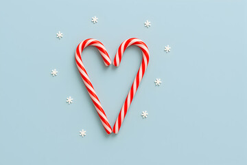 Two candy canes are arranged in a heart shape with snowflakes on a light blue background for christmas, christmas
