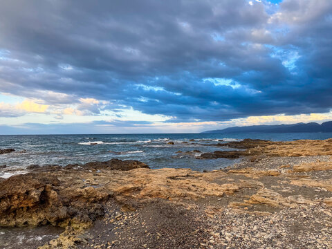 Calm evening by the rocky shore as waves gently crash under an expansive sky filled with dramatic clouds near the coastline - Powered by Adobe