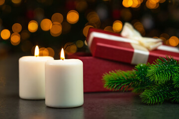 Close up of lit candles and red box with Christmas gift on background of Christmas tree with golden garland lights. Christmas and new year holiday decor