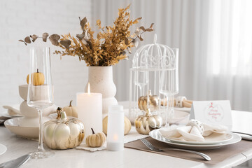 Elegant table serving with pumpkins and burning candles for Thanksgiving dinner in light room