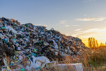 Garbage and plastic waste pile up in a landfill while the sun sets in the background, showcasing...