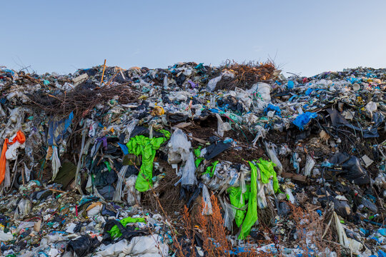 A vast landfill site full of various types of waste, including plastic, clothing, and other debris, highlights pollution and ecological issues