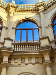 Beautiful architectural details of a historic building in a sunny afternoon, showcasing intricate carvings and large windows reflecting blue sky