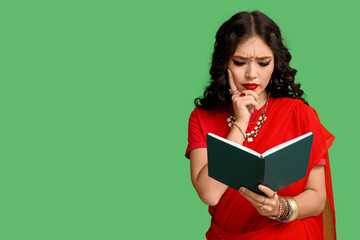 Fototapeta premium Beautiful thoughtful Indian woman in sari reading book on green background