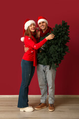 Beautiful young couple with Christmas tree on red background