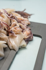The mottled, translucent skin of the raw squid rings contrasts with the uniform gray background of the Teflon pan, highlighting their marine freshness