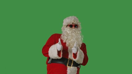 Santa Claus with a white curly beard, wearing a red suit and sunglasses, points his fingers at camera on a green background. Perfect for Christmas themed compositions, advertisements, holiday layouts.